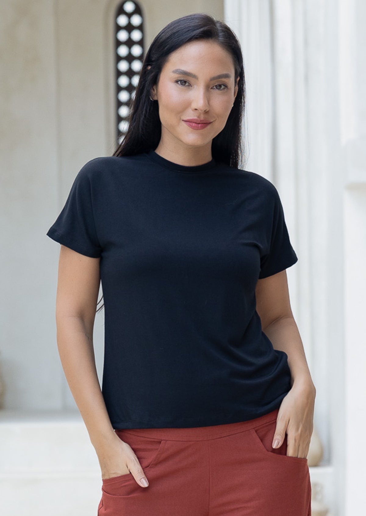 Woman wearing a black crewneck t-shirt and rust coloured pants with hands in pockets