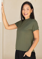 Woman wearing an olive green rayon t-shirt with one hand rested on wall