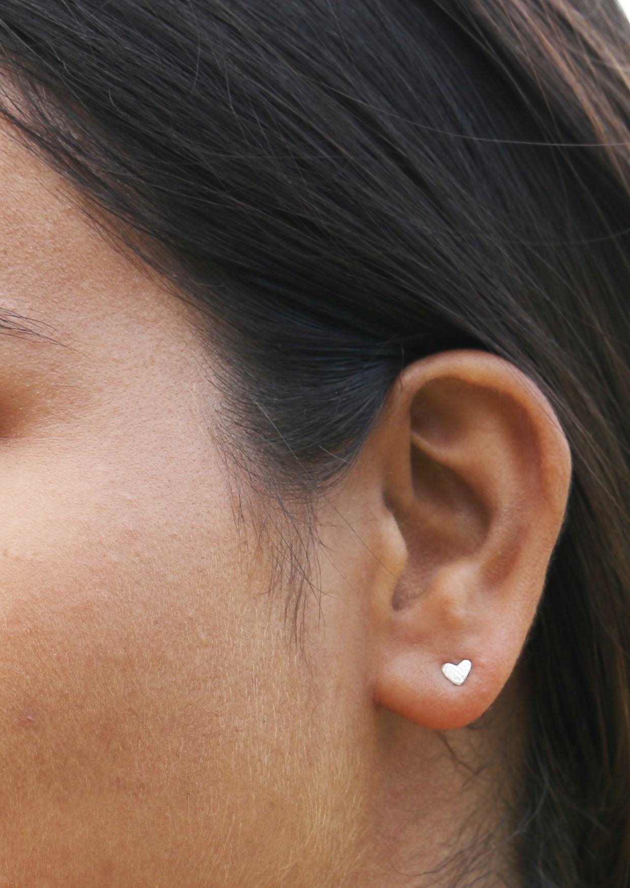 Woman wearing small silver heart shaped studs with textured design