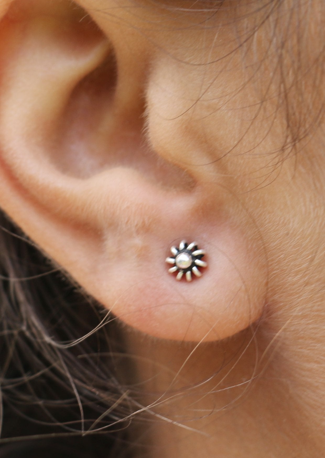 Close-up of an ear with a small sterling silver dandelion studs with delicate wire spring petals and central silver ball 