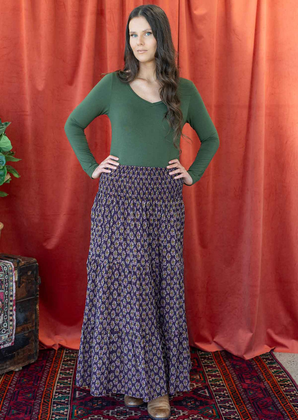 Woman wearing a cotton maxi skirt with wide elastic shirred waistband, in dark purple based floral pattern.