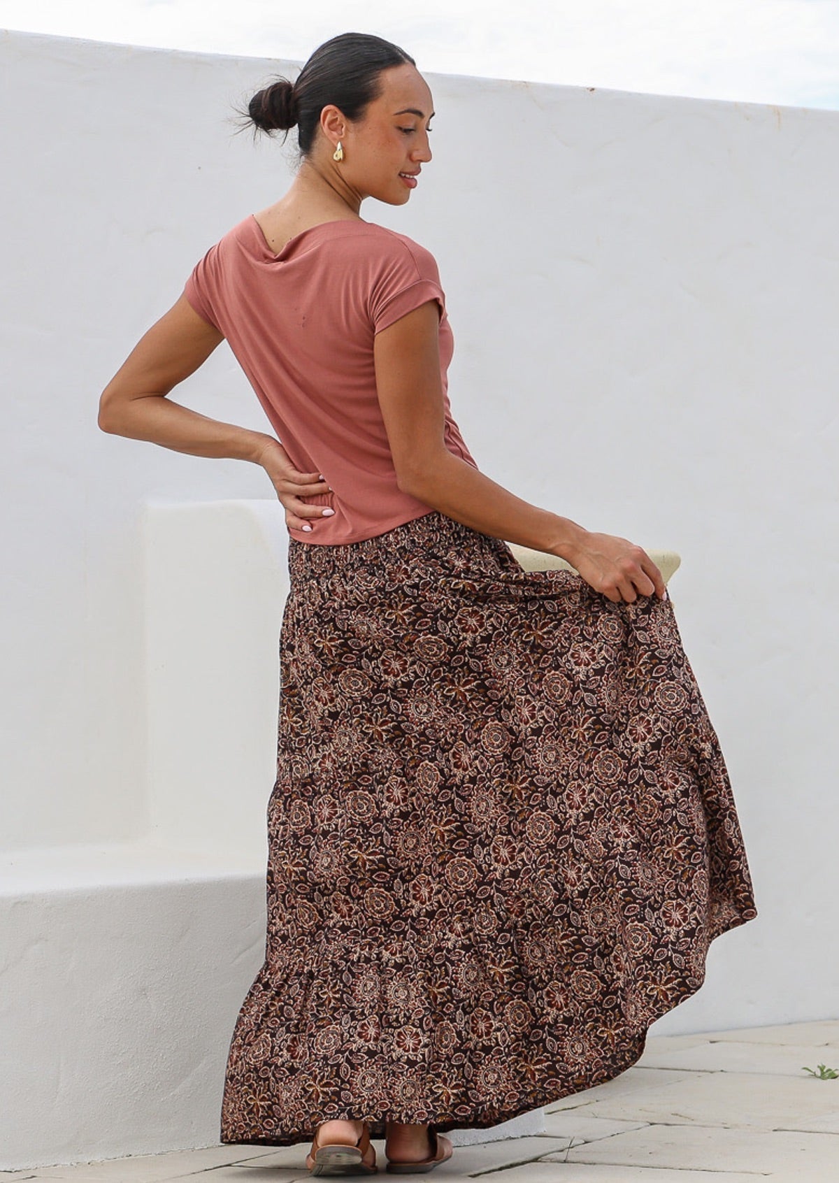 Model standing in back pose wearing a three tiered, floral print cotton maxi skirt with wide neck stretch top in dusty rose.