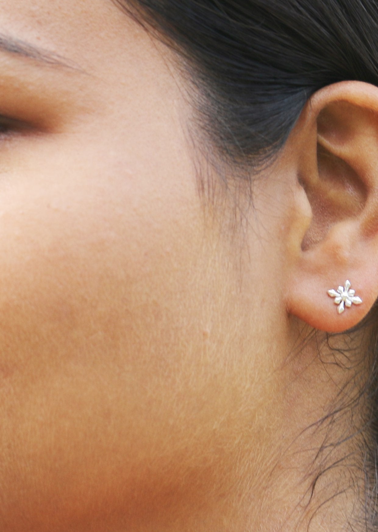 Close up of an ear wearing a silver star flower shaped studs with secure butterfly backs  