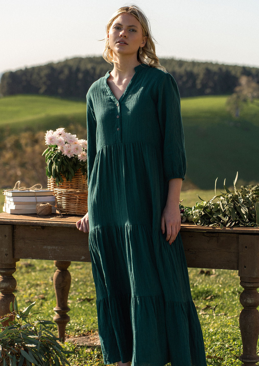 Women in deep teal cotton maxi dress in the country in front of old rustic table covered in flowers