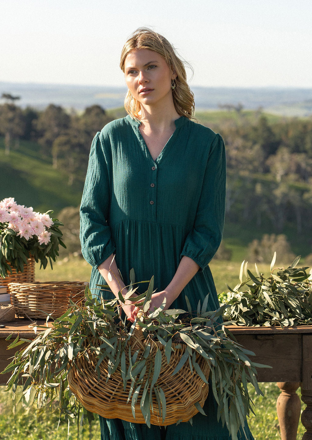 Women in deep teal cotton maxi dress in the country in front of old rustic table covered in gum leaves and flowers
