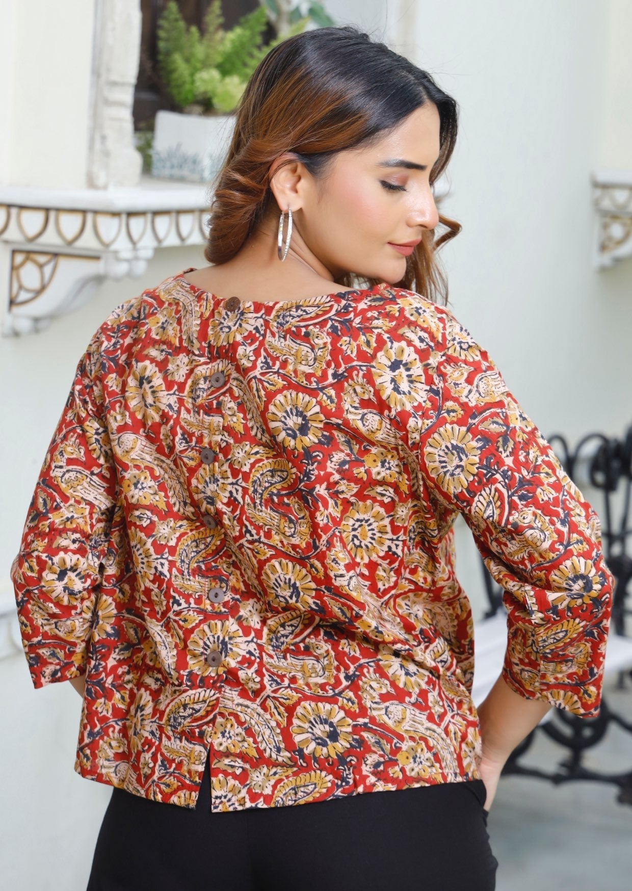 Woman stands showing the back of the cotton top with decorative buttons down the centre of the back.