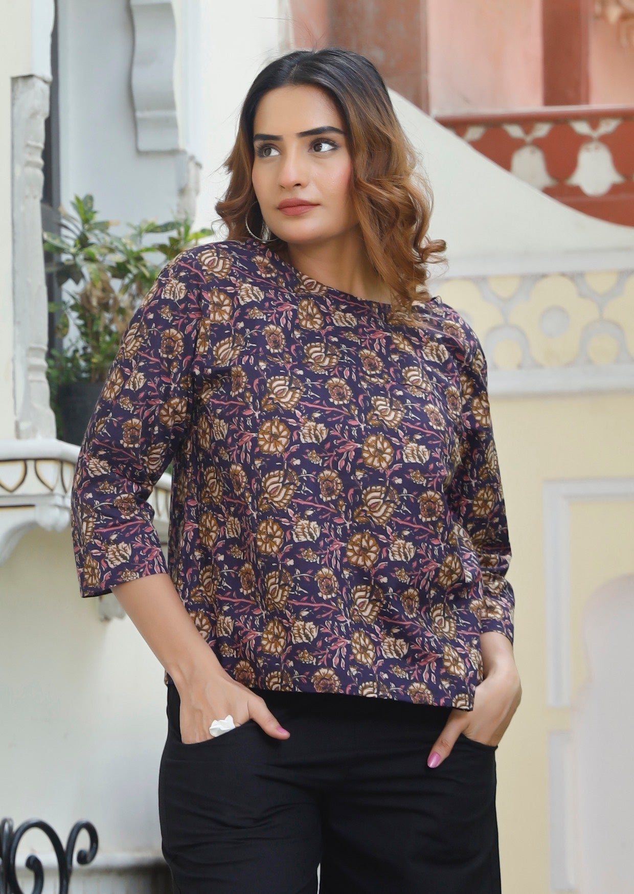 Woman wears cotton lose fit top in pink, cream and light brown floral print on dark purple base.