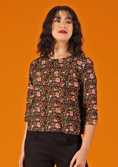 woman with dark hair and red lipstick in boxy cotton blouse, black base with earthy floral design