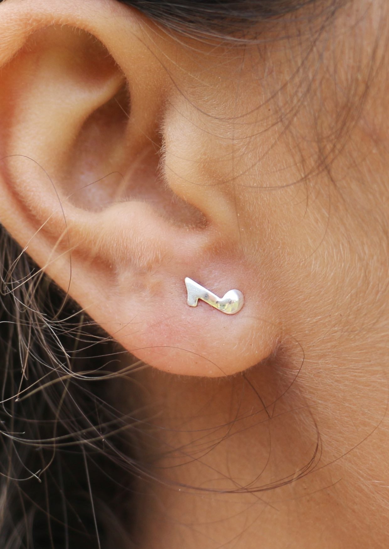 Sterling silver eight note quaver studs displayed on a woman's ear with butterfly backs 