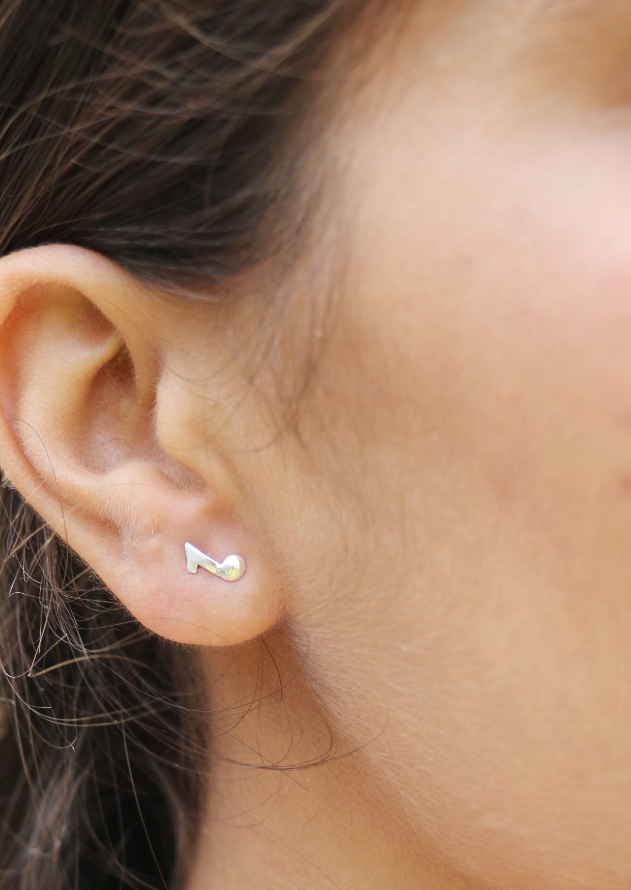 Close-up of an ear wearing a small silver  quaver, eighth note stud earrings with secure butterfly backs