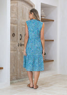 Back view of woman wearing a blue floral dress standing in a room with wooden doors and shelves.