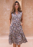 Woman wearing a knee length cotton sleeveless dress with buttoned bodice and  two tiered skirt in taupe based floral print.