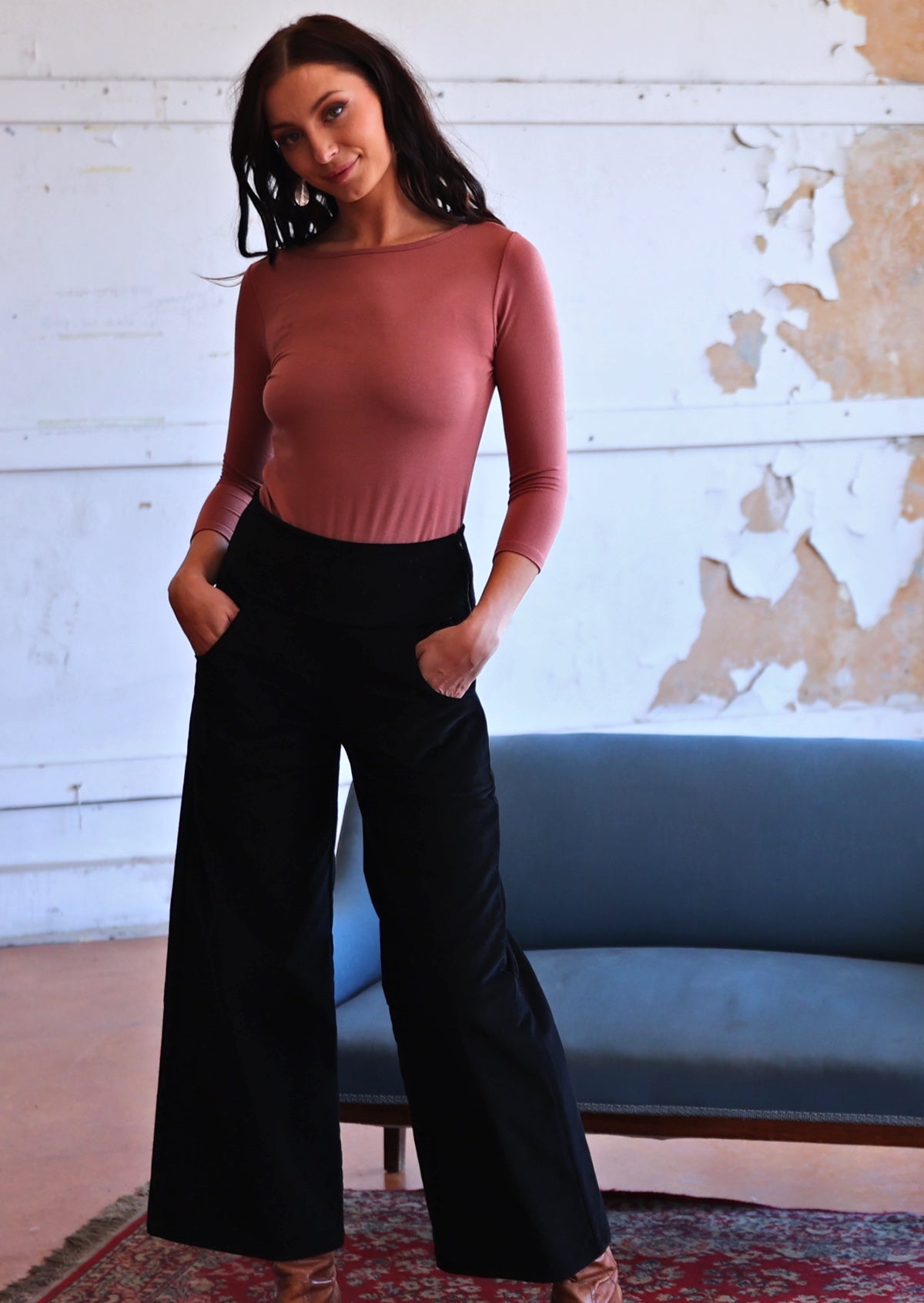 Woman wearing black corduroy wide legged pants with pink top with hands in pockets 