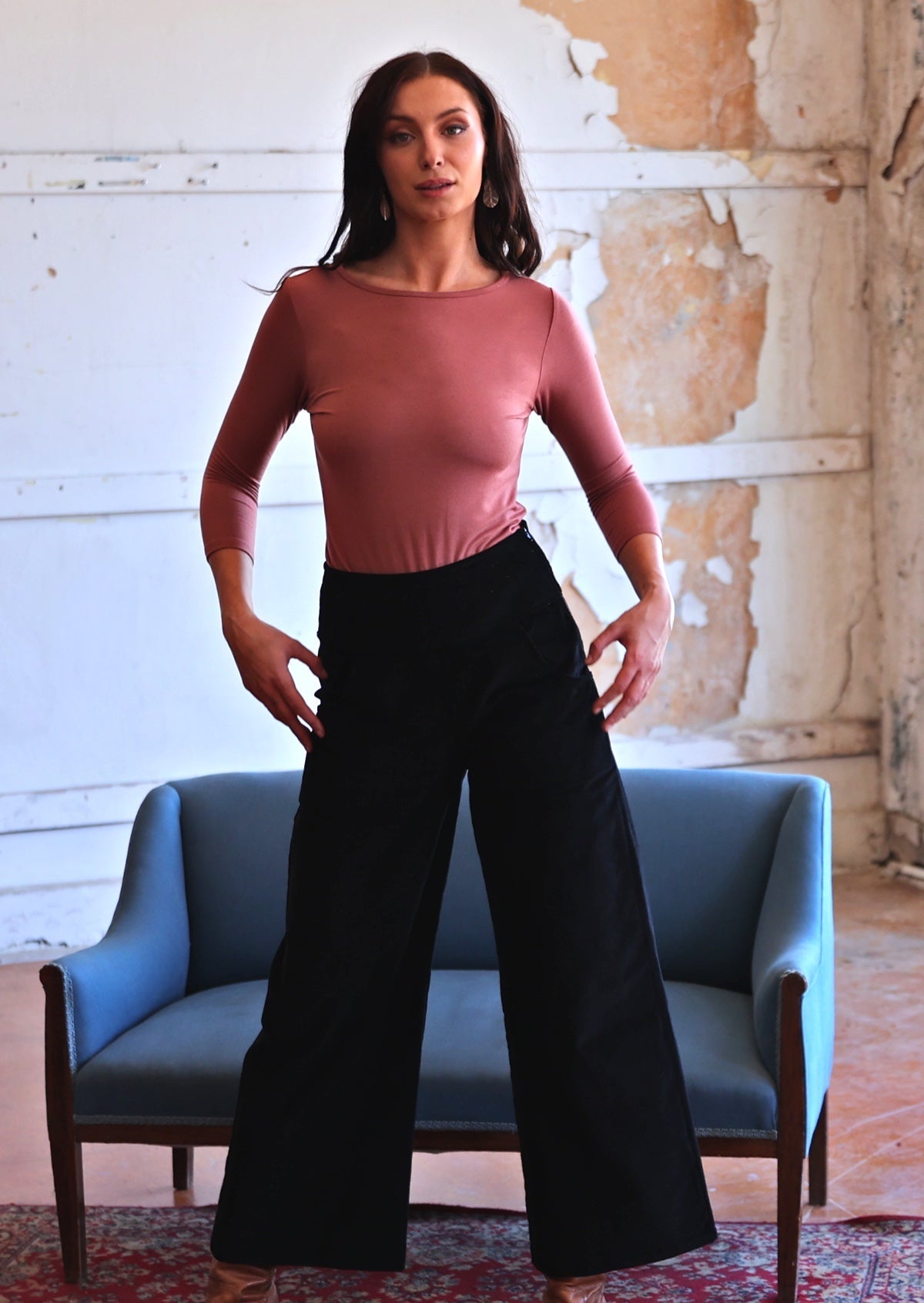 Woman wearing black corduroy wide legged pants with pink top with hands near pockets 