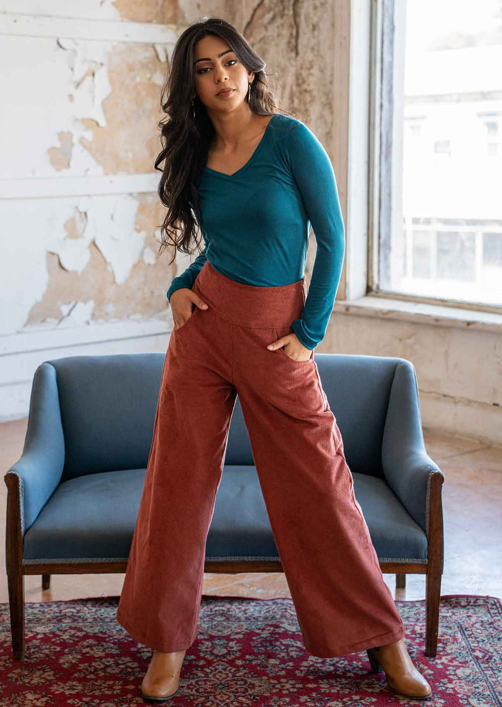 Model poses in terracotta coloured wide leg corduroy pants with a wide waistband, with her hands in pockets