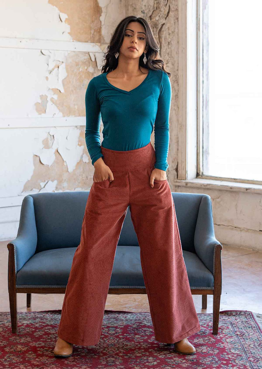 Model poses in wide leg corduroy pants in terracotta colour, with her hands in pockets