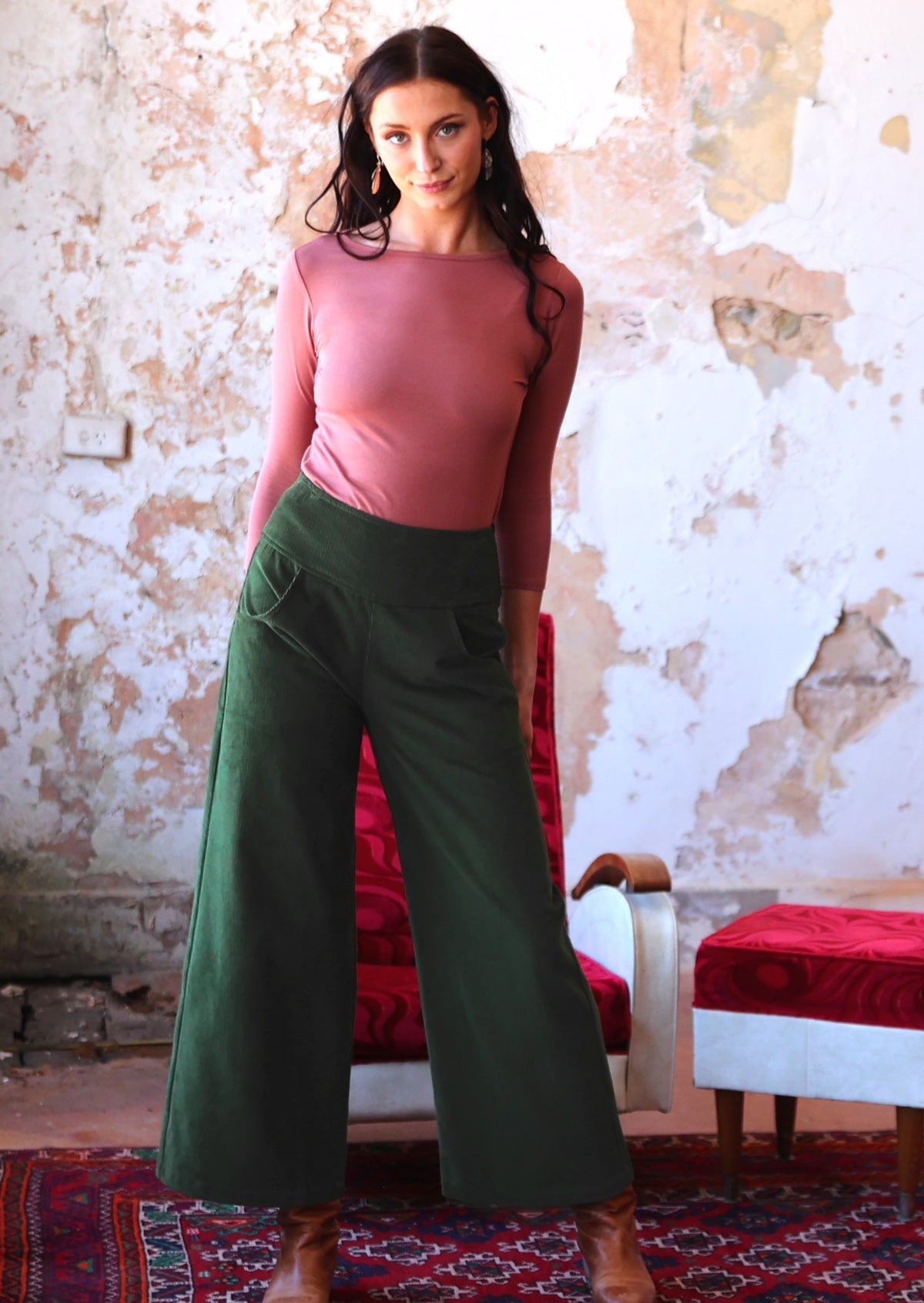 woman wearing long sleeve pink boat neck top and green corduroy pants in old building 