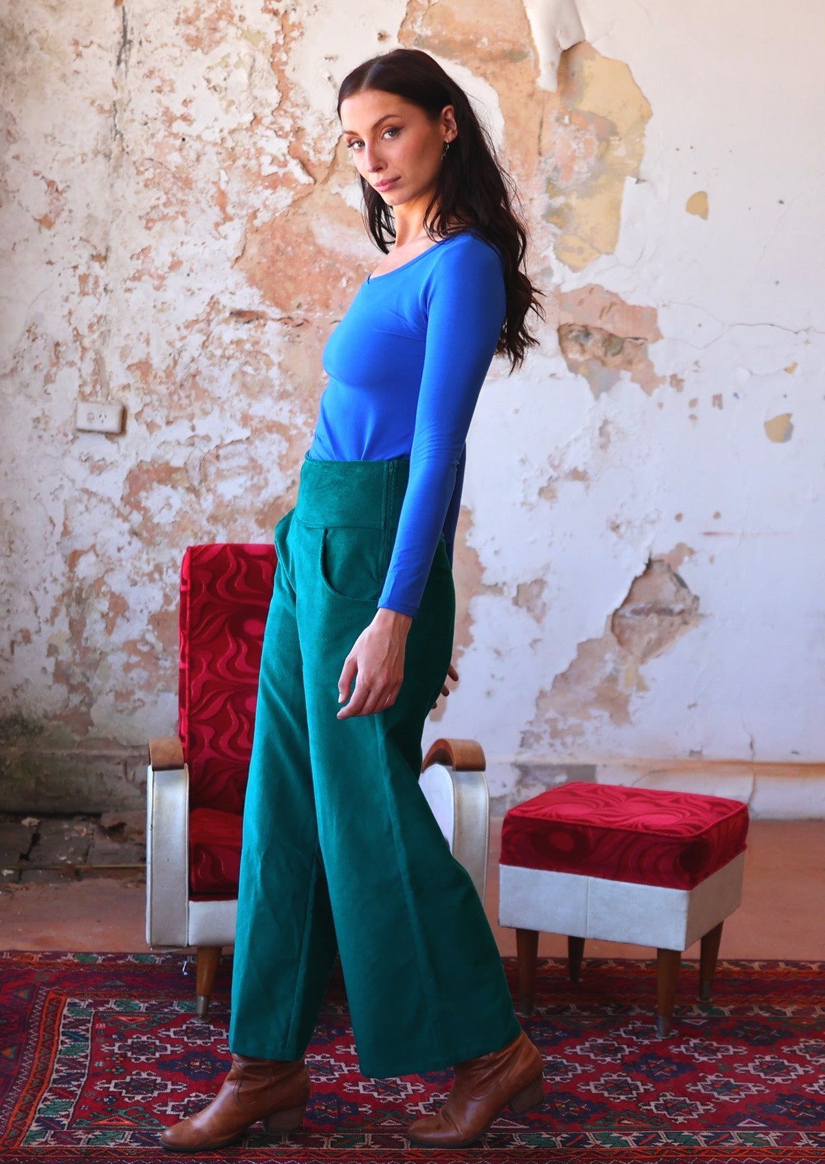 Woman stands side on in electric blue long sleeve top with teal wide leg corduroy pants with a side zip and pockets