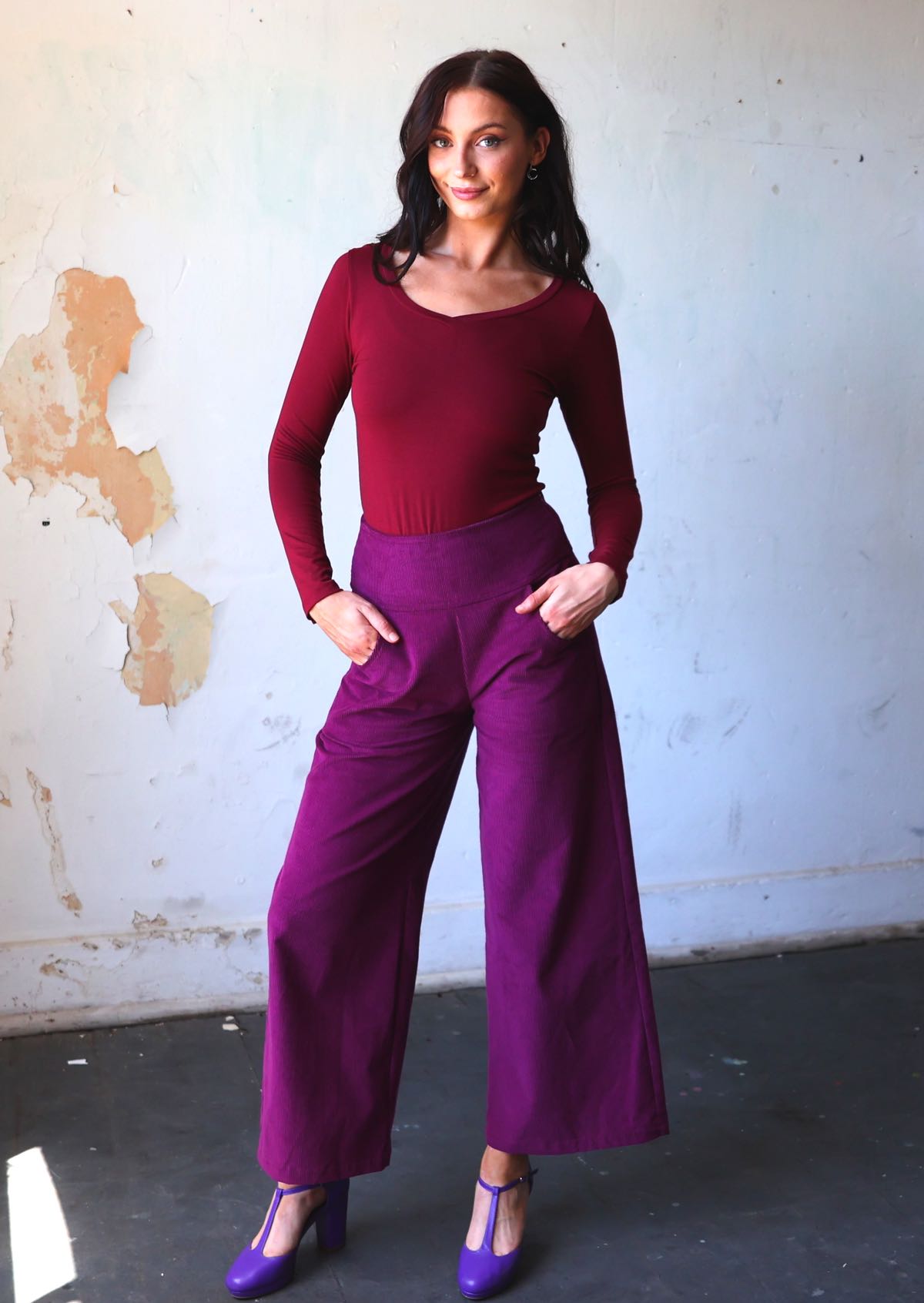 Model wears plum purple corduroy wide leg pants with her hands in pockets, paired with a maroon long sleeve top