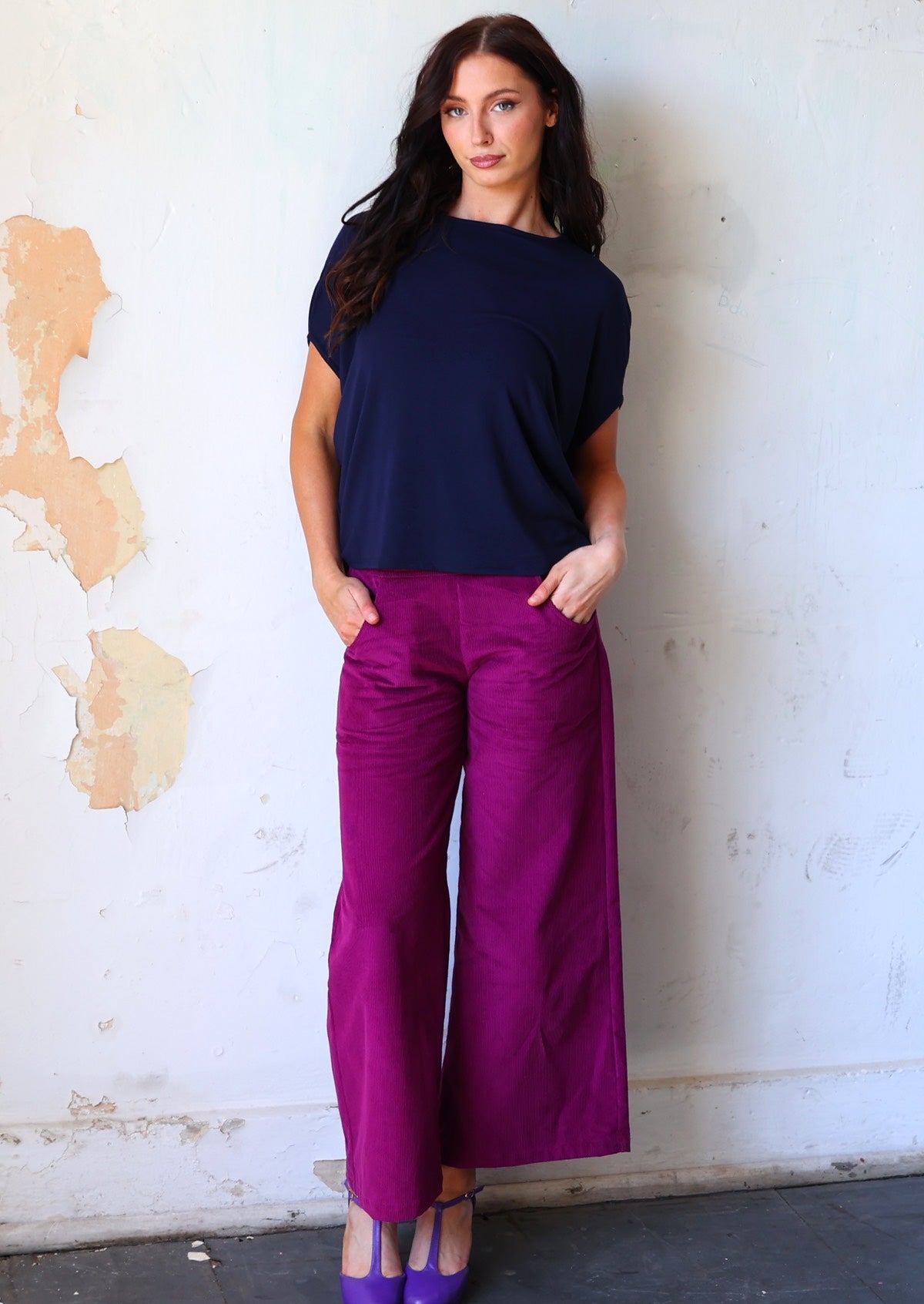 Woman wears plum purple wide leg corduroy pants with hands in pockets, paired with a dark navy batwing top