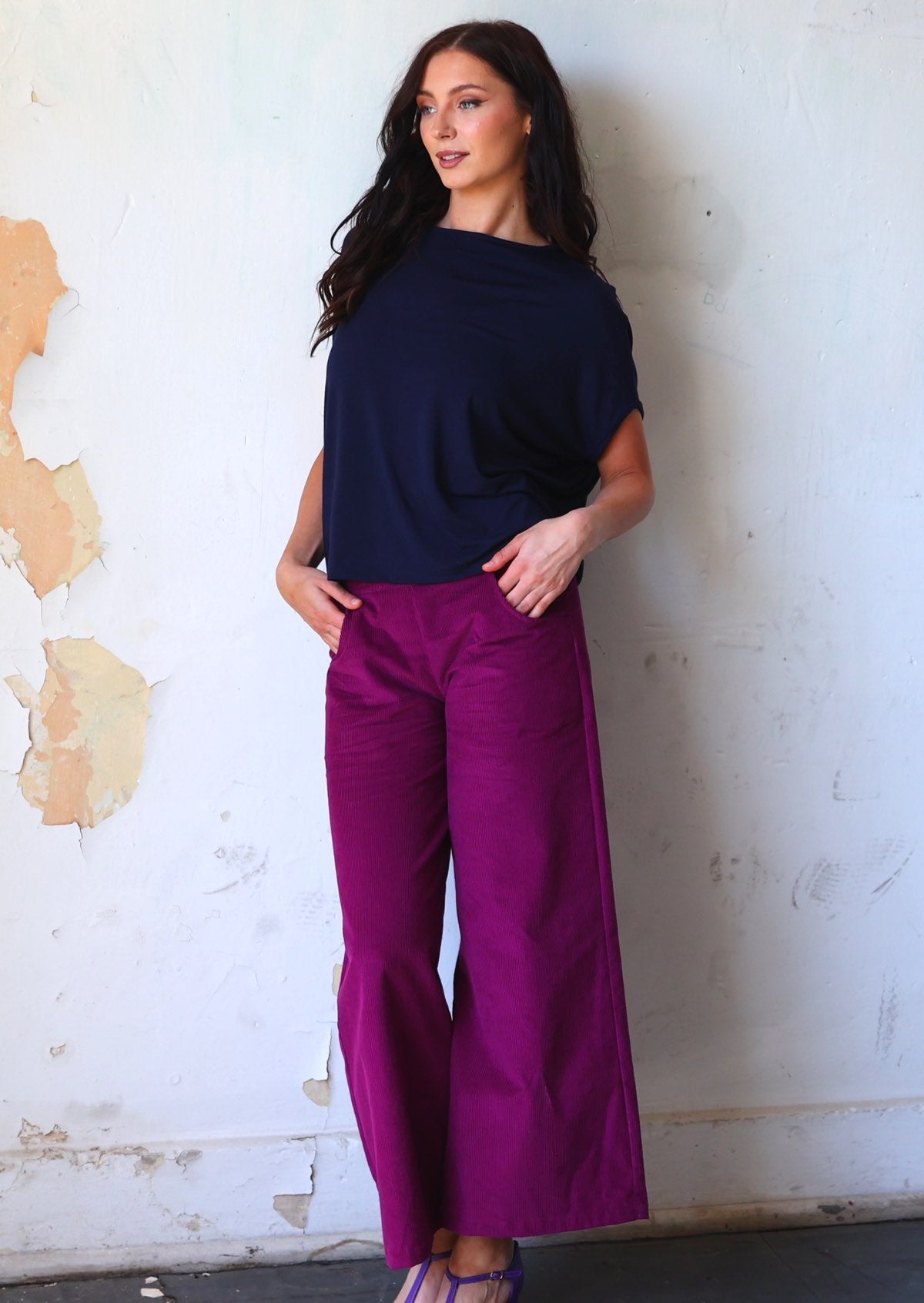 Model wears plum purple corduroy wide leg pants with her hands in pockets, paired with a dark navy batwing top