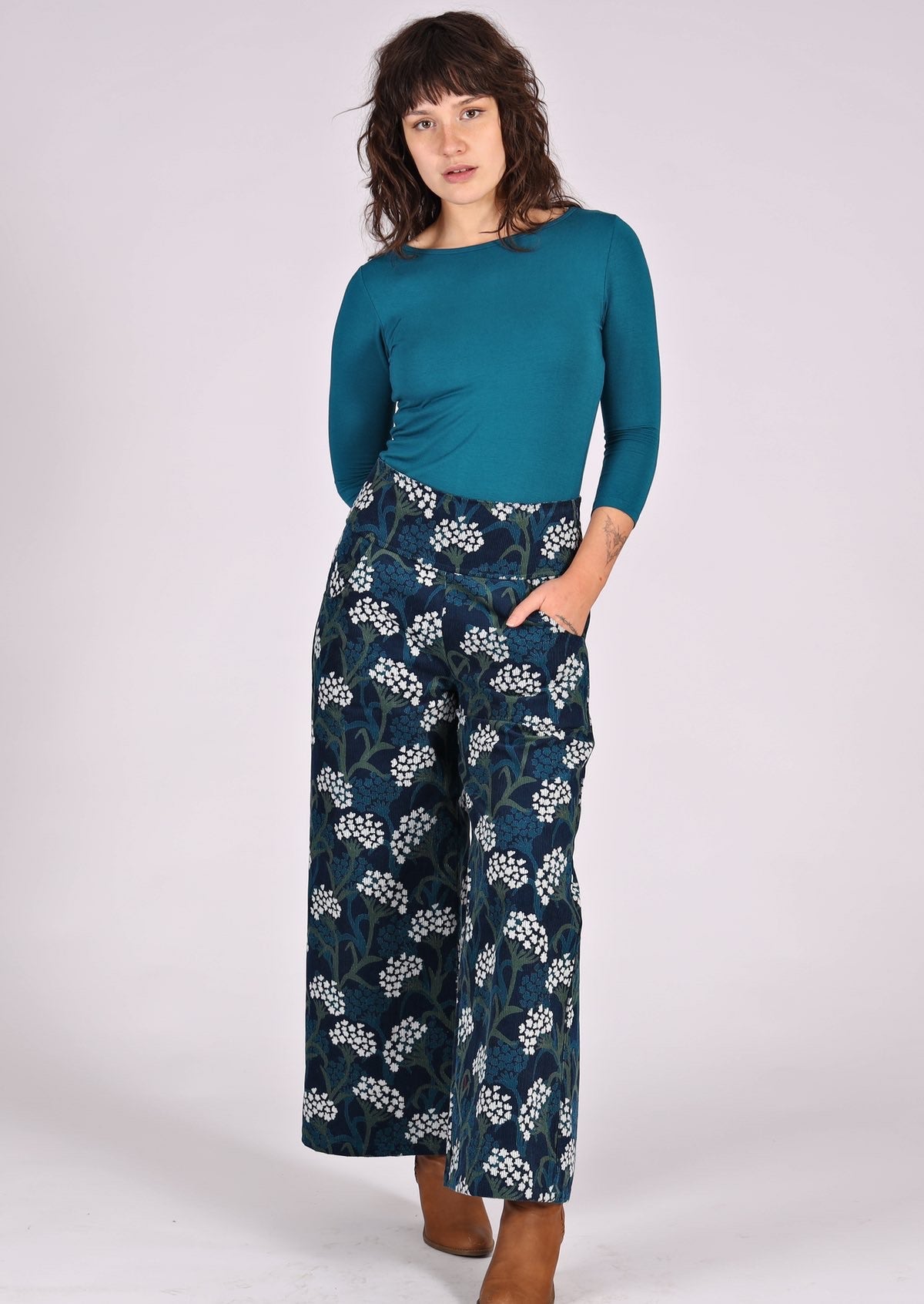 Model poses in cotton corduroy wide leg pants paired with a teal stretch top, with hand in pocket