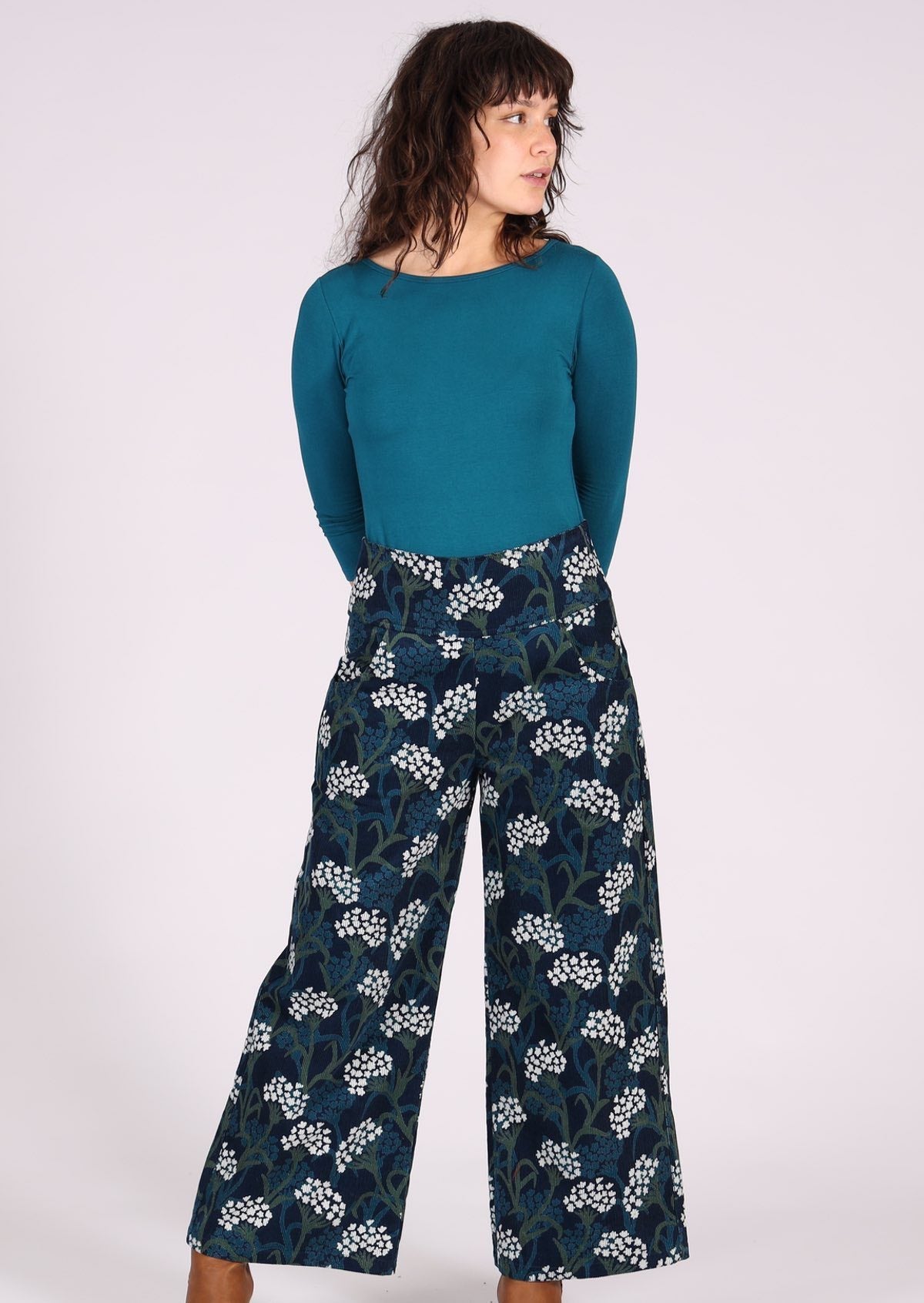Woman wears wide leg corduroy pants with a wide waistband, in a floral print on dark blue base