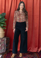 woman wearing black corduroy wide leg pants with hand on hip, paired with printed cotton blouse and ankle boots