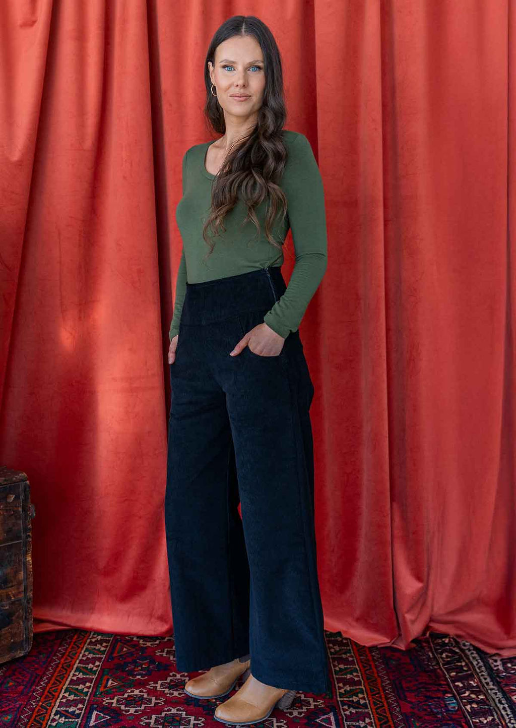 woman wearing black corduroy wide leg pants with hand in pocket with long sleeve green top 