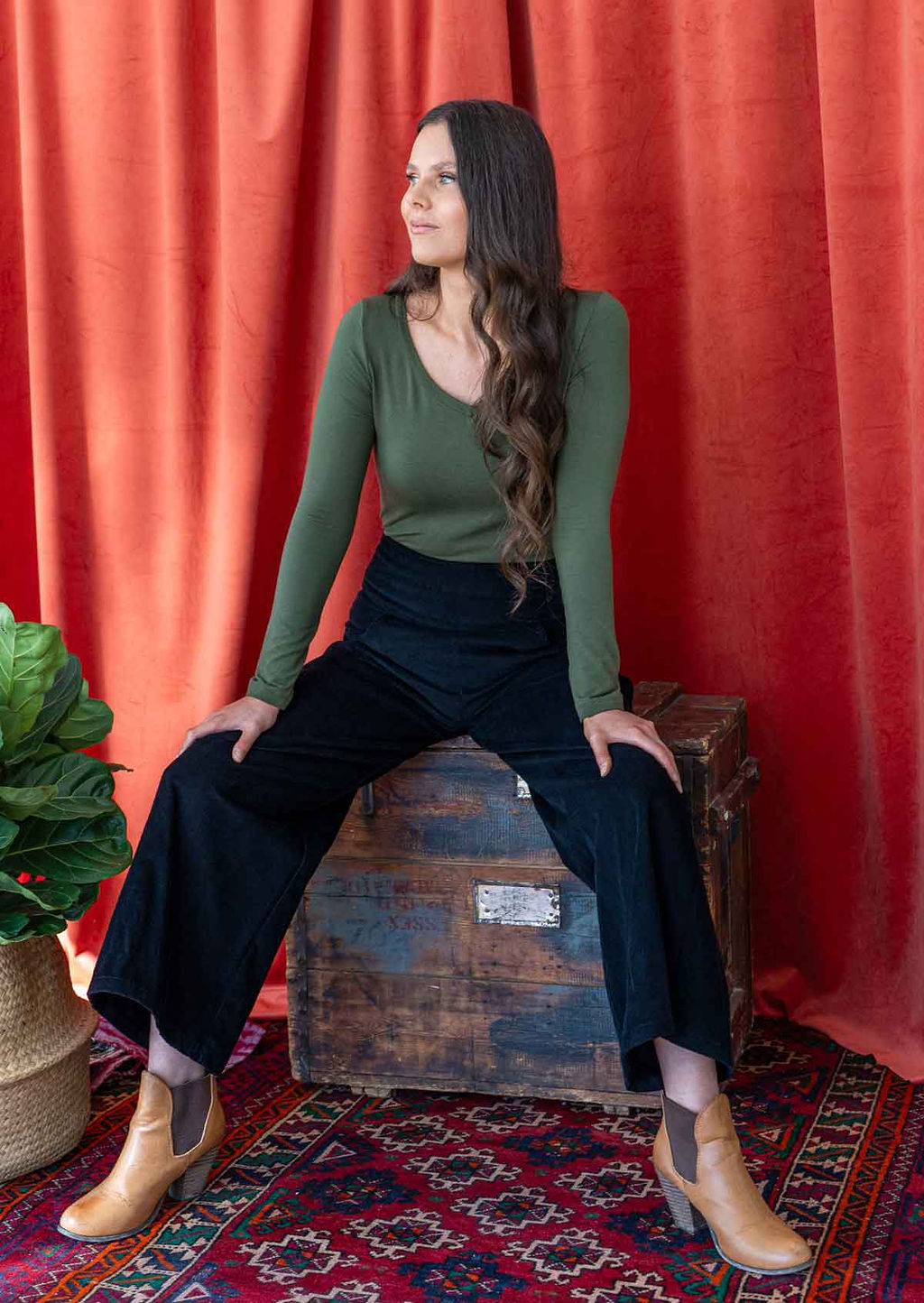 woman wearing black corduroy wide leg pants sitting on crate with long sleeve green top 