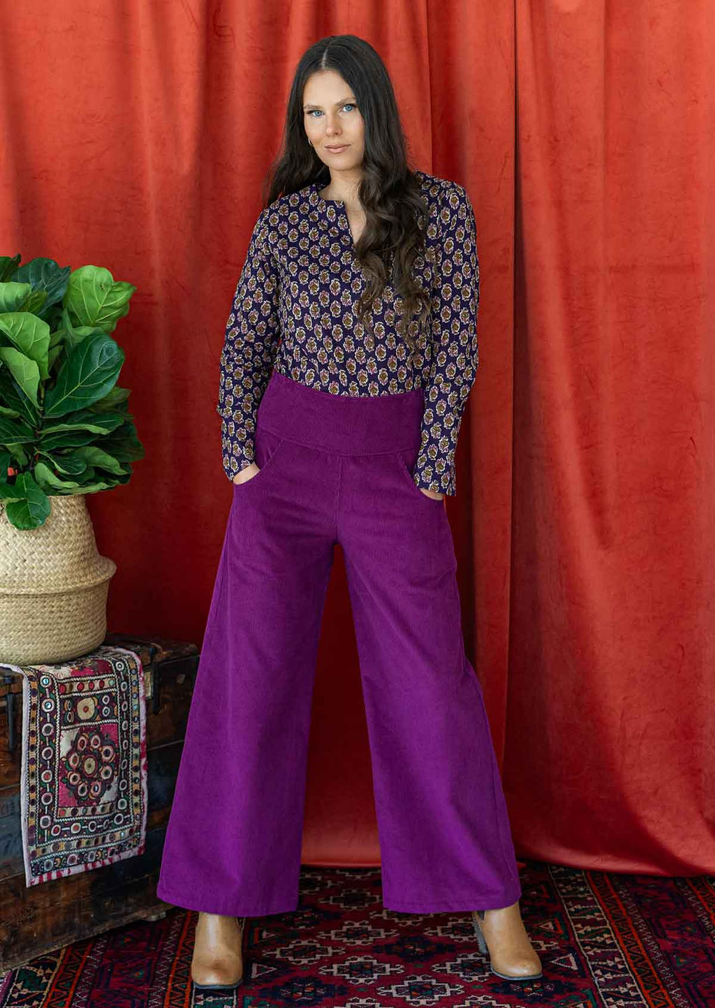 woman wears purple corduroy wide leg pants with her hands in pockets, paired with a long sleeve purple cotton blouse 