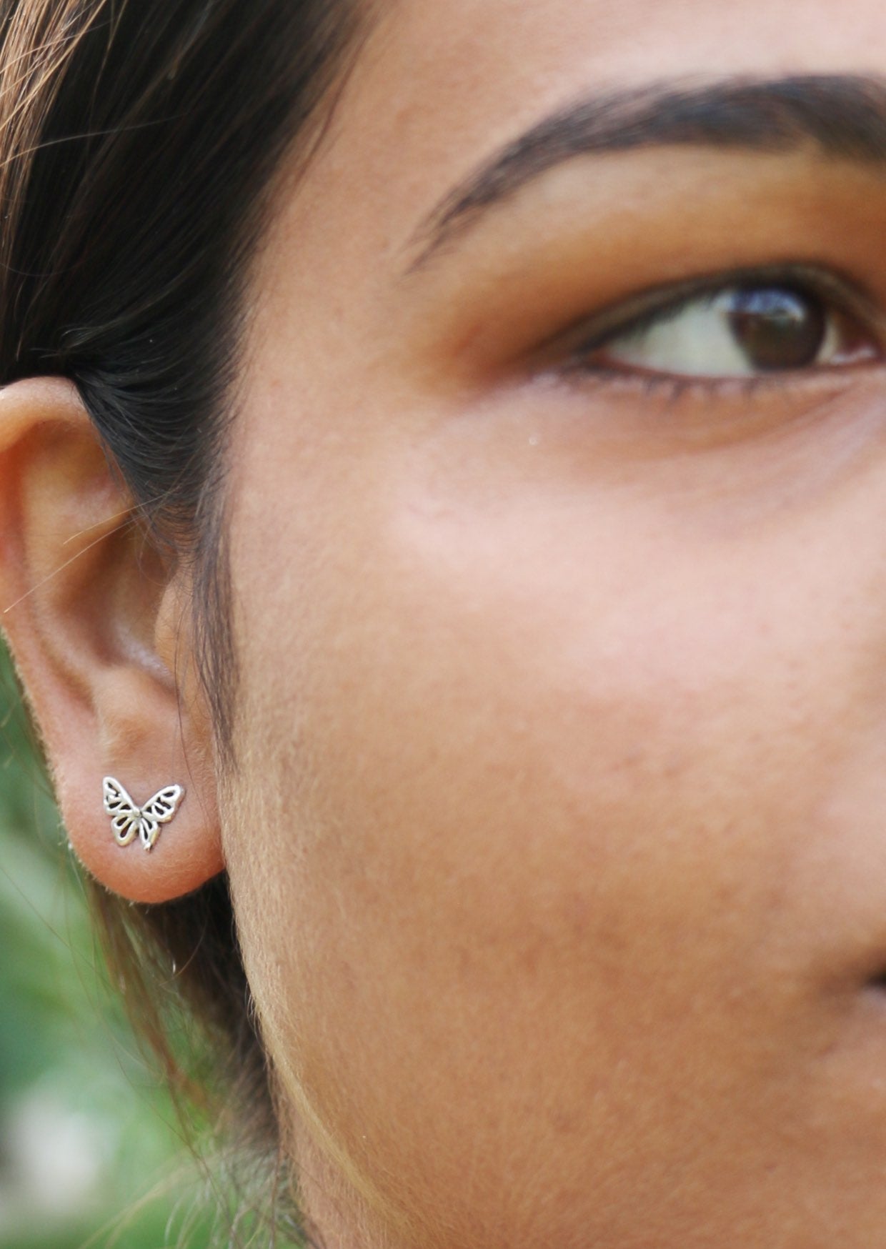 Close-up of a person wearing butterfly-shaped studs featuring intricate cutout details