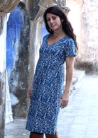 Woman stands sideways in cotton over the knee short sleeve dress with white floral print on a blue base