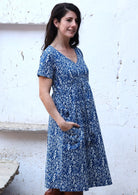Model wears cotton over the knee length short sleeve dress with a V-neckline in white floral print on a blue base
