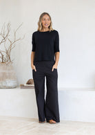 Woman wearing a black relaxed fit rayon top with black cotton pants standing in a minimalistic room