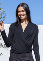 Woman wearing a black long sleeve crossover top against a blue sky background