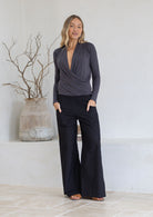 Woman wearing a dark grey stretch rayon long sleeve crossover top with hands in pockets of black pants