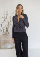Woman wearing a long sleeve crossover grey top with a plunging V-neckline and black pants