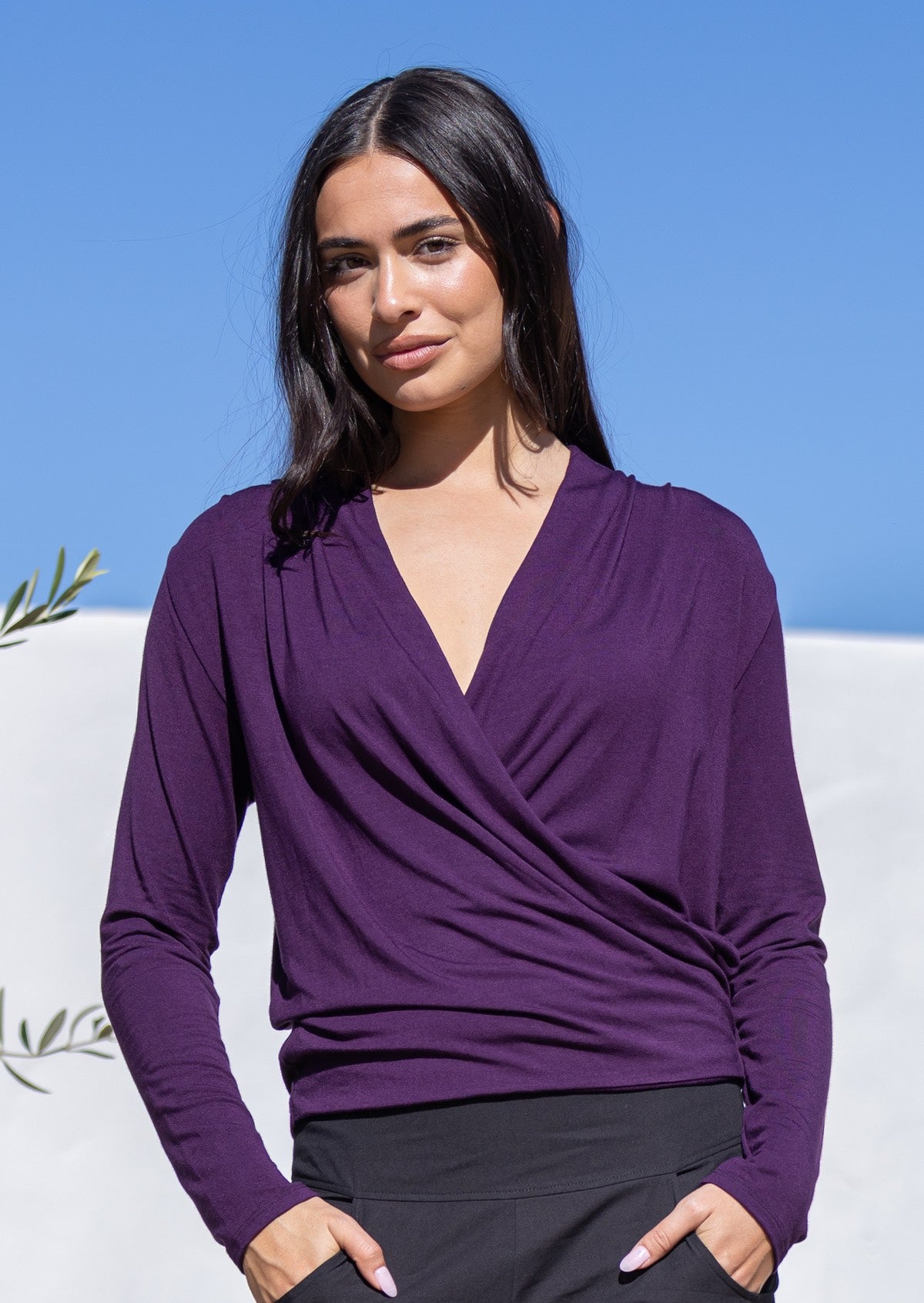 Woman wearing a purple long sleeve false wrap top with a V-neckline against a blue sky background