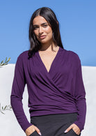 Woman wearing a purple long sleeve false wrap top with a V-neckline against a blue sky background