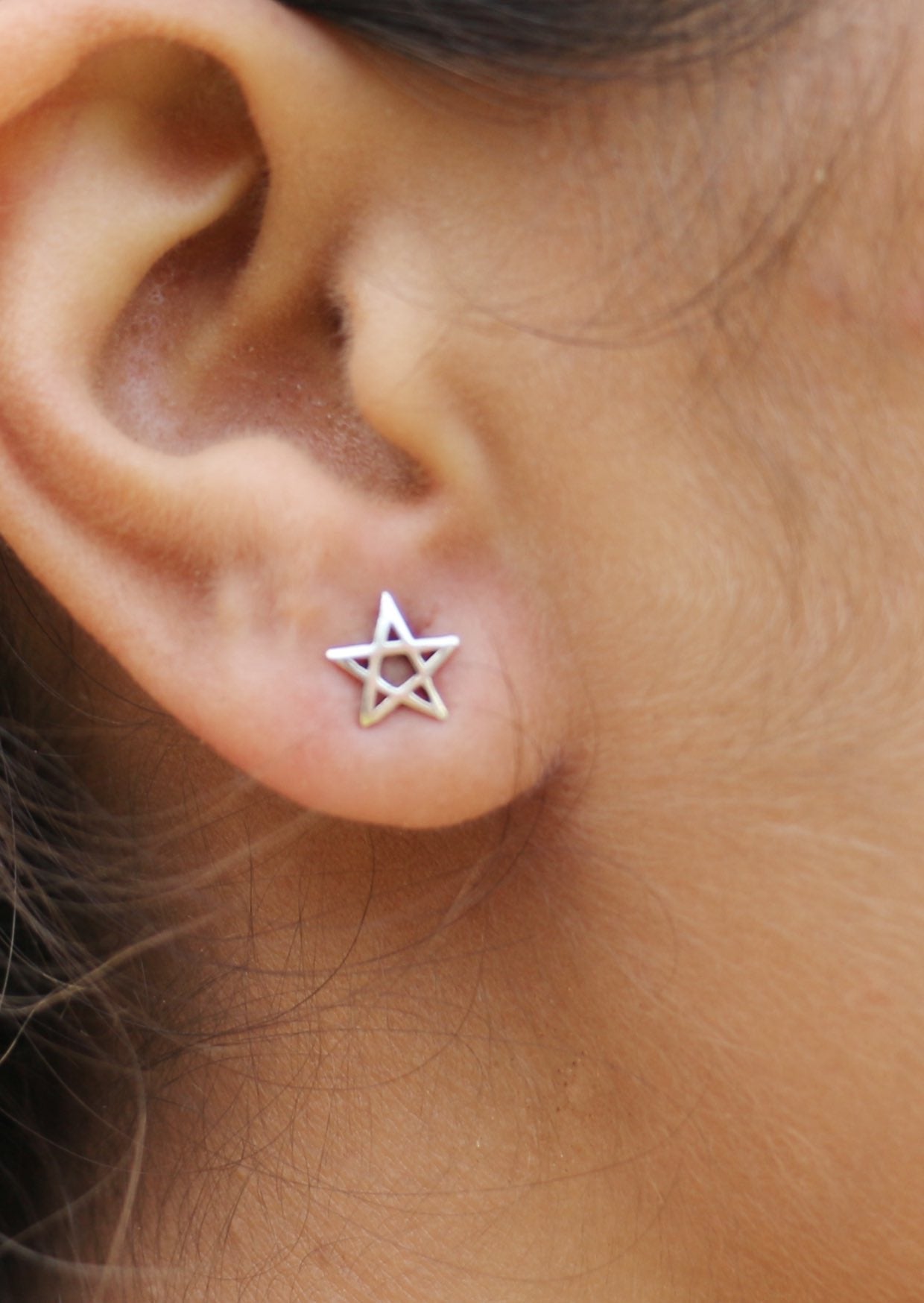 Silver five point star-shaped studs on a person's ear