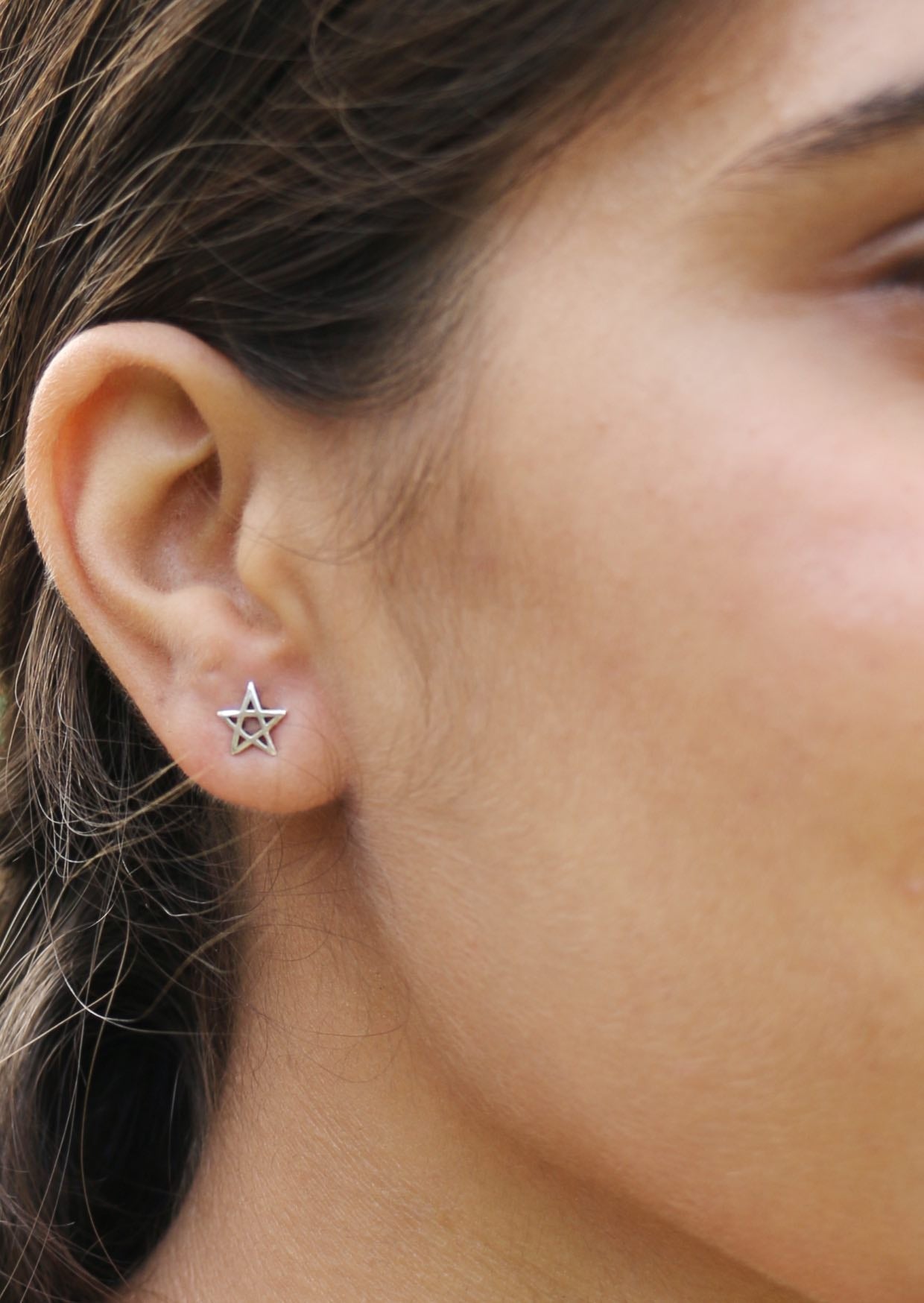 Close-up of an ear wearing a sterling silver five point star studs with a cutout design