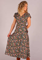 Model standing one hand behind back and other hand holding side of skirting of navy floral rayon wrap maxi sundress 