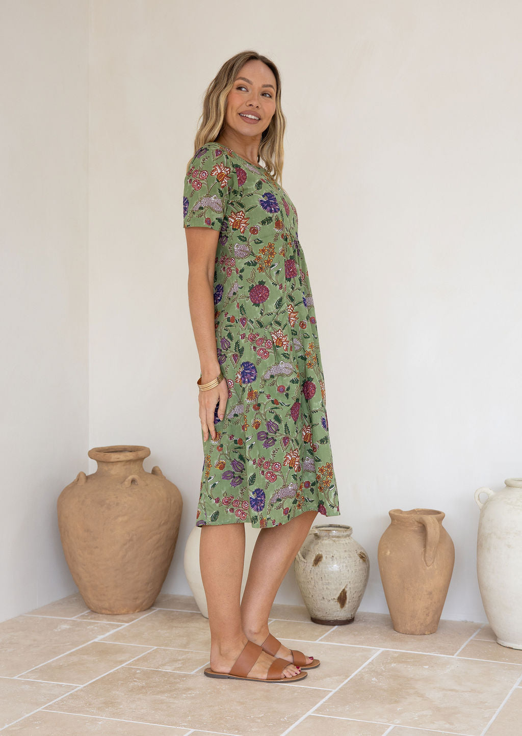 Woman wearing a green based floral print knee length cotton dress.