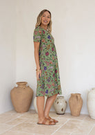 Woman wearing a green based floral print knee length cotton dress.