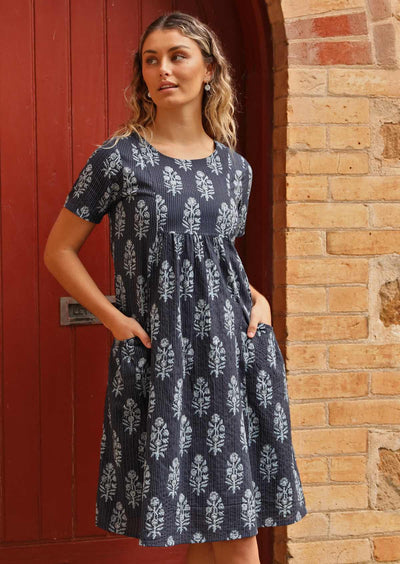 Woman standing in front of church door with navy blue cotton Indian print summer dress with hand in pockets