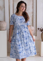 Woman wearing a blue floral cotton dress which sits below the knee.