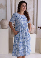 Woman wearing a blue floral cotton dress standing in a neutral setting.