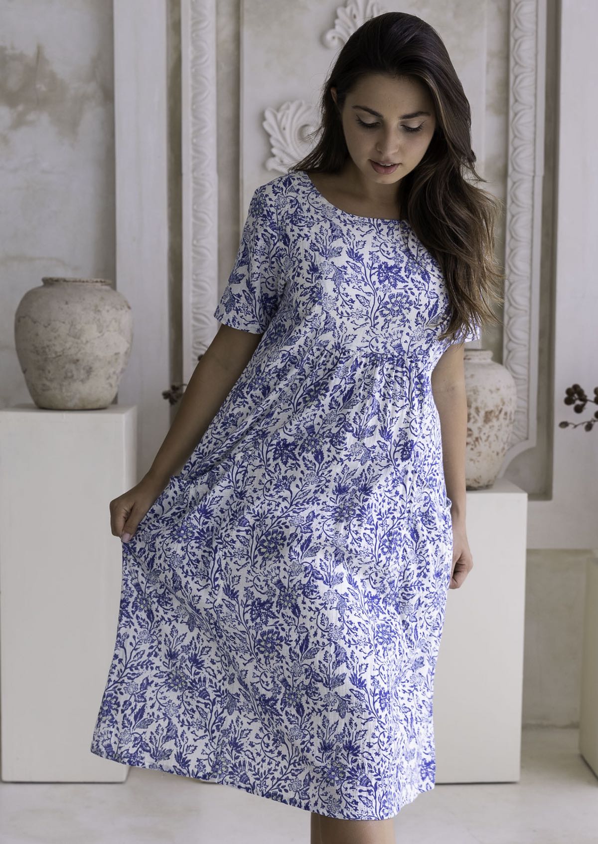 Woman wearing a blue floral cotton dress which sits below the knees in a neutral setting.