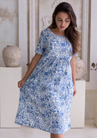 Woman wearing a blue floral cotton dress which sits below the knees in a neutral setting.